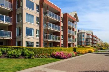 Modern apartment buildings with landscaped walkway and colorful shrubs under a blue sky